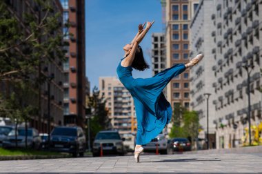 Açık havada dans eden mavi elbiseli güzel bir Asyalı balerin. Şehir manzarası