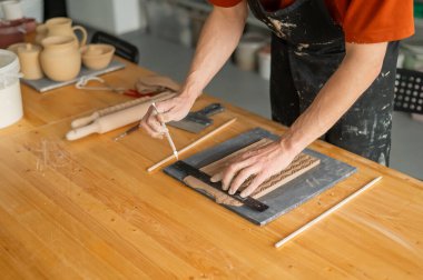 Çömlekçi ellerinin yakın plan görüntüsü. Yuvarlanmış kilden bir parça kesiyorlar.