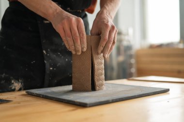 Bir adamın elleri kilden bir silindir yaratıyor.