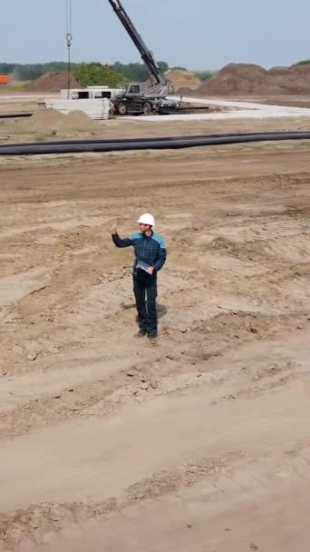 一名戴头盔的男子在建筑工地进行技术监督 无人机垂直视频 — 图库视频影像