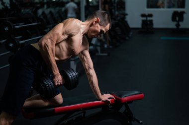 Gömleksiz bir adam spor salonunda dambıl sırasına dizer.