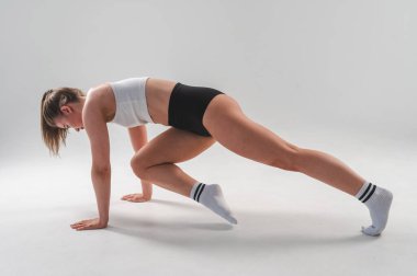 Beyaz arka planda kalas egzersizi yapan şortlu atletik kadın.