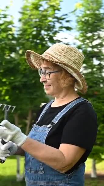Şapkalı Tulumlu Yaşlı Bir Kadının Portresi Bir Bahçe Aleti Tutuyor — Stok video