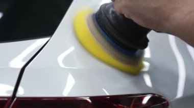 Bir tamirci beyaz bir arabanın yüzeyini parlatır.