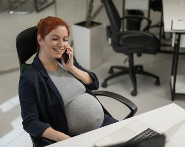 Ofiste cep telefonu kullanan hamile kadın.
