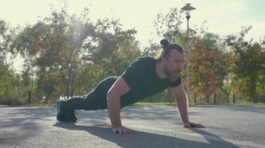 Uzun saçlı sakallı adam spor sahasında şınav çekiyor.