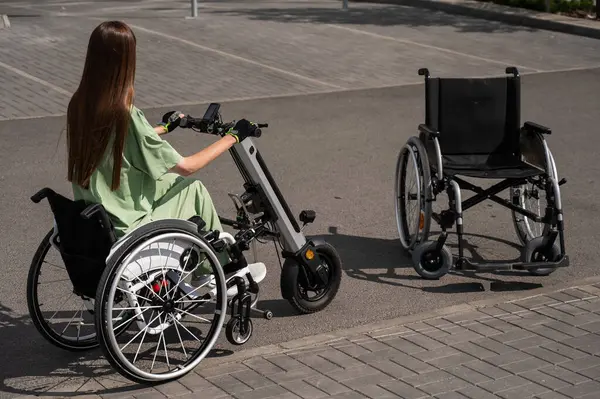 stock image Woman in wheelchair with assistive device for manual control next to classic wheelchair. Electric handbike