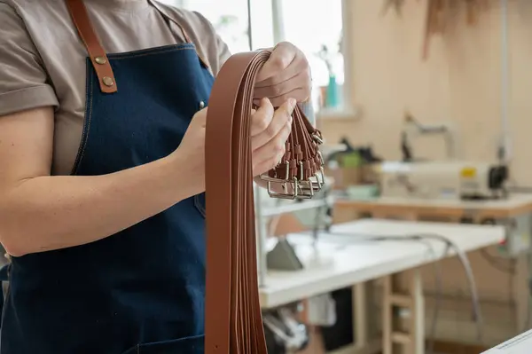Close-up of a Caucasian womans hands making genuine leather belts in a workshop