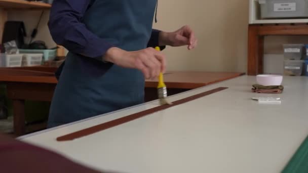 職人は不浸透で革ベルトをコーティングするためにブラシを使用します — ストック動画