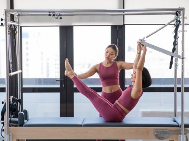 Cadillac reformcusu eğitmeniyle pilates yapan Asyalı kadın.