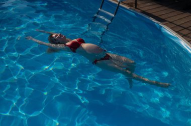 Havuzda kırmızı bikinili hamile bir kadın.