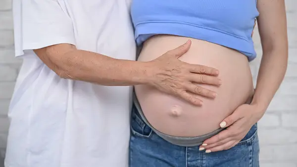 An elderly woman touches the belly of her pregnant daughter. Close-up