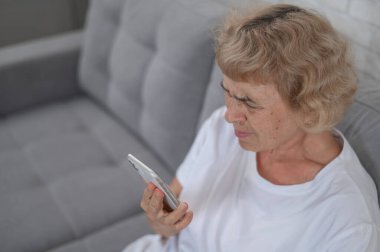 Yaşlı beyaz bir kadın miyoptan muzdarip ve akıllı telefondan mesaj okumaya çalışıyor.