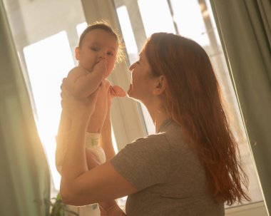 Beyaz bir kadın yeni doğmuş oğlunu nazikçe kaldırır.