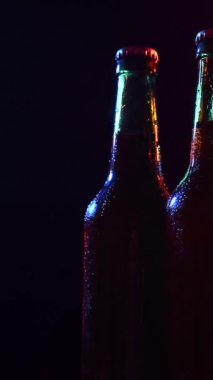 Siyah arka planda renkli ışıkta dönen üç şişe bira. Dikey video
