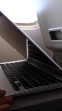 Maskeli meçhul kadın uçuş sırasında pencerenin yanında otururken dizüstü bilgisayarda çalışıyor. Bir seyahatte serbest çalışan. Dikey video