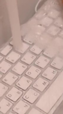 Beyaz bilgisayar klavyesini köpüklü süngerle yıkayan kadın. Dikey video