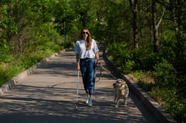 Kör kadın parkta rehber köpekle yürüyor.