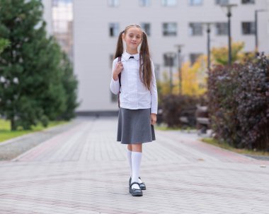 Beyaz üniformalı ve sırt çantalı bir kız okuldan ayrılıyor.