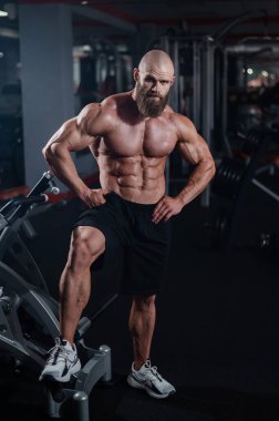 Şort giymiş kaslı kel adam. Vücut geliştirici spor salonunda vücudunu gösteriyor.