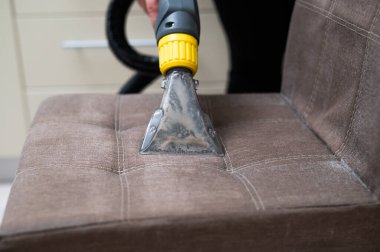 Kadın, elektrikli süpürgeyle kumaş sandalyesini temizliyor.