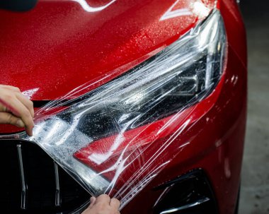 Usta, kırmızı bir arabanın farına vinil film uyguluyor.