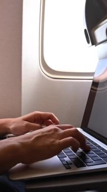 Maskeli meçhul kadın uçuş sırasında pencerenin yanında otururken dizüstü bilgisayarda çalışıyor. Bir seyahatte serbest çalışan. Dikey video
