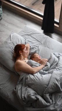 Kızıl saçlı beyaz bir kadının, küçük oğluyla yatakta yatışının en güzel görüntüsü. Dikey video