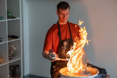 Çömlekçinin biri çömlekçi çarkında gaz yakan bir sürahi yakıyor.