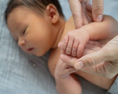 Yeni doğmuş bir çocuk annesinin parmağını tutar. Ellerin yakın çekimi