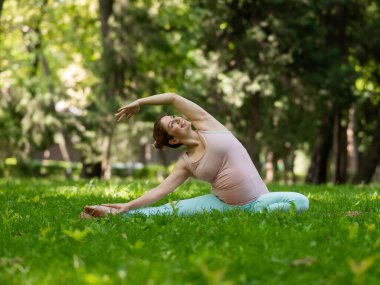 Parkta yoga yapan hamile, beyaz bir kadın. Yanal eğim