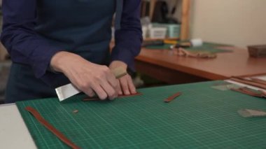 Deri işçisi bir atölyedeki kemerden bir parça deri kesiyor.