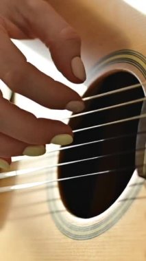 Kadın ellerinin akustik gitarla yakın çekimi. Kız gitar çalmayı öğreniyor. Dikey video