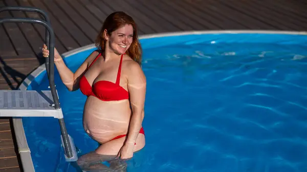 stock image A red-haired pregnant woman goes down the stairs into the pool outdoors