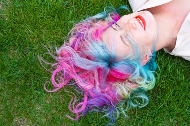 Kafkasyalı kadının yeşil çimlerin üzerinde uzanan çok renkli saçları var.