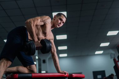 Gömleksiz bir adam spor salonunda dambıl sırasına dizer.