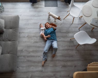 Beyaz kadın, oğlu ve Jack Russell Terrier köpeğiyle yerde yatıyor.