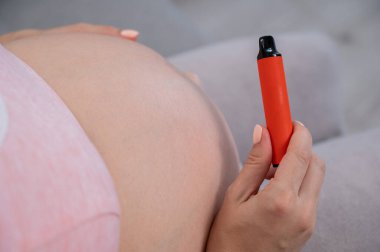 Hamile bir kadın kanepede otururken sigara içiyor. Karna yakın çekim.