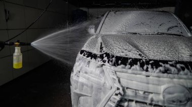 Oto yıkamada siyah arabaya köpük süren bir adam.