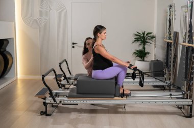 Kafkasyalı hamile kadın, bireysel bir eğitmenle ıslah makinesinde pilates egzersizi yapıyor.