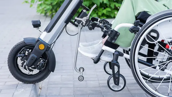 Tekerlekli sandalyedeki yüzü olmayan ve manuel kontrol için yardımcı bir aleti olan bir kadın. Elektrikli bisiklet.