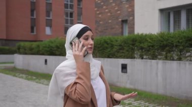 Açık havada akıllı telefondan konuşan tesettürlü genç kadın.
