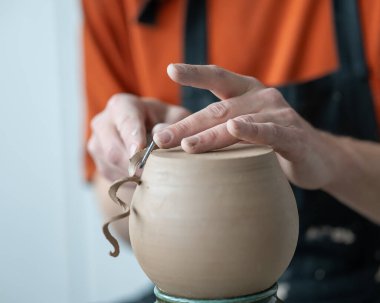 A potter works with a tool on a potters wheel. Close-up of a mans hands