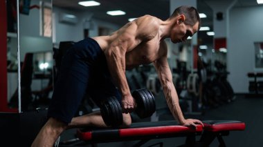 Gömleksiz bir adam spor salonunda dambıl sırasına dizer.