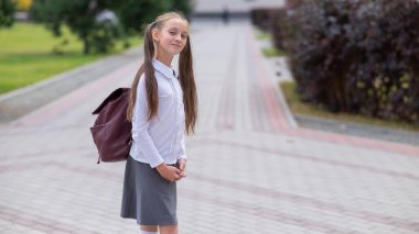 Beyaz üniformalı ve sırt çantalı bir kız okuldan ayrılıyor.