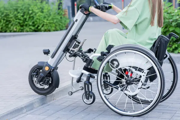 Stock image A faceless woman in a wheelchair with an assistive device for manual control. Electric handbike