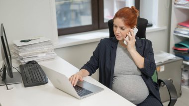 Ofiste cep telefonu kullanan hamile kadın.