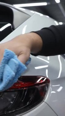 Bir adam mikrofiber bir bezle beyaz bir arabanın yüzeyini siliyor. Dikey video