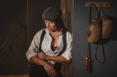 Peaky Blinders tarzı erkek kıyafeti giymiş beyaz bir kadın retro spor salonunda poz veriyor.