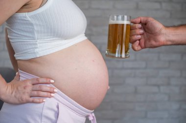A man clinks a bottle of beer with a pregnant womans belly clipart